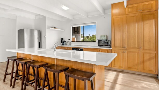 A modern kitchen with a large island, bar stools, wooden cabinets, and a view of the outdoors. - Hiddensee in Central Cowes (Cowes)