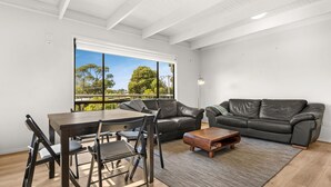 A modern living room with a dining area, featuring a large window with a view of trees and a clear sky. - Hiddensee in Central Cowes (Cowes)