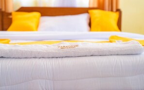 Una cama bien tendida con un edredón blanco y una toalla blanca con el texto 'TAKEOVER' bordado.