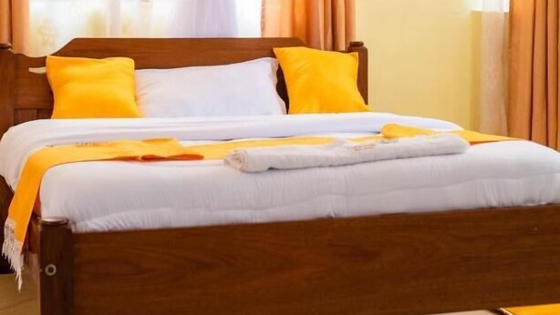 A bed with a wooden frame, white bedding, and yellow pillows. - Takeover Restaurant & Accommodation (Kisumu)