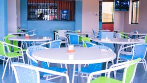 A restaurant with round tables and chairs, a bar area, and a TV screen. - Takeover Restaurant & Accommodation (Kisumu)