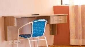 A small room with a single chair, a desk, and a window with curtains. - Takeover Restaurant & Accommodation (Kisumu)