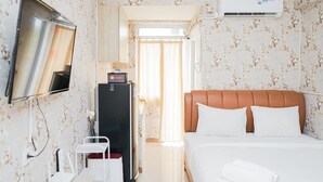 Een hotelkamer met een bed, een televisie, een bureau, een koelkast en een airconditioning.