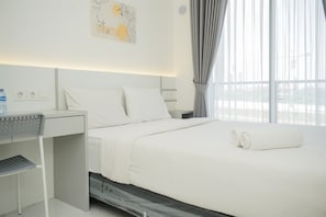 A modern hotel room with a neatly made bed, a desk, and a large window with curtains. - Fully Furnished And Tidy Studio Sky House Bsd Apartment (Pagedangan)