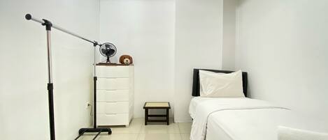 A hotel room with a bed, a small table, a dresser, and a ceiling fan.