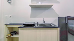 A compact kitchen with a sink, a stove, and a shelf above the counter. - Elegant And Comfy Studio Barsa City Apartment (Depok)
