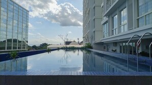A modern hotel with a swimming pool, large windows, and a clear sky. - Cozy Studio At Mataram City Apartment (Ngaglik)