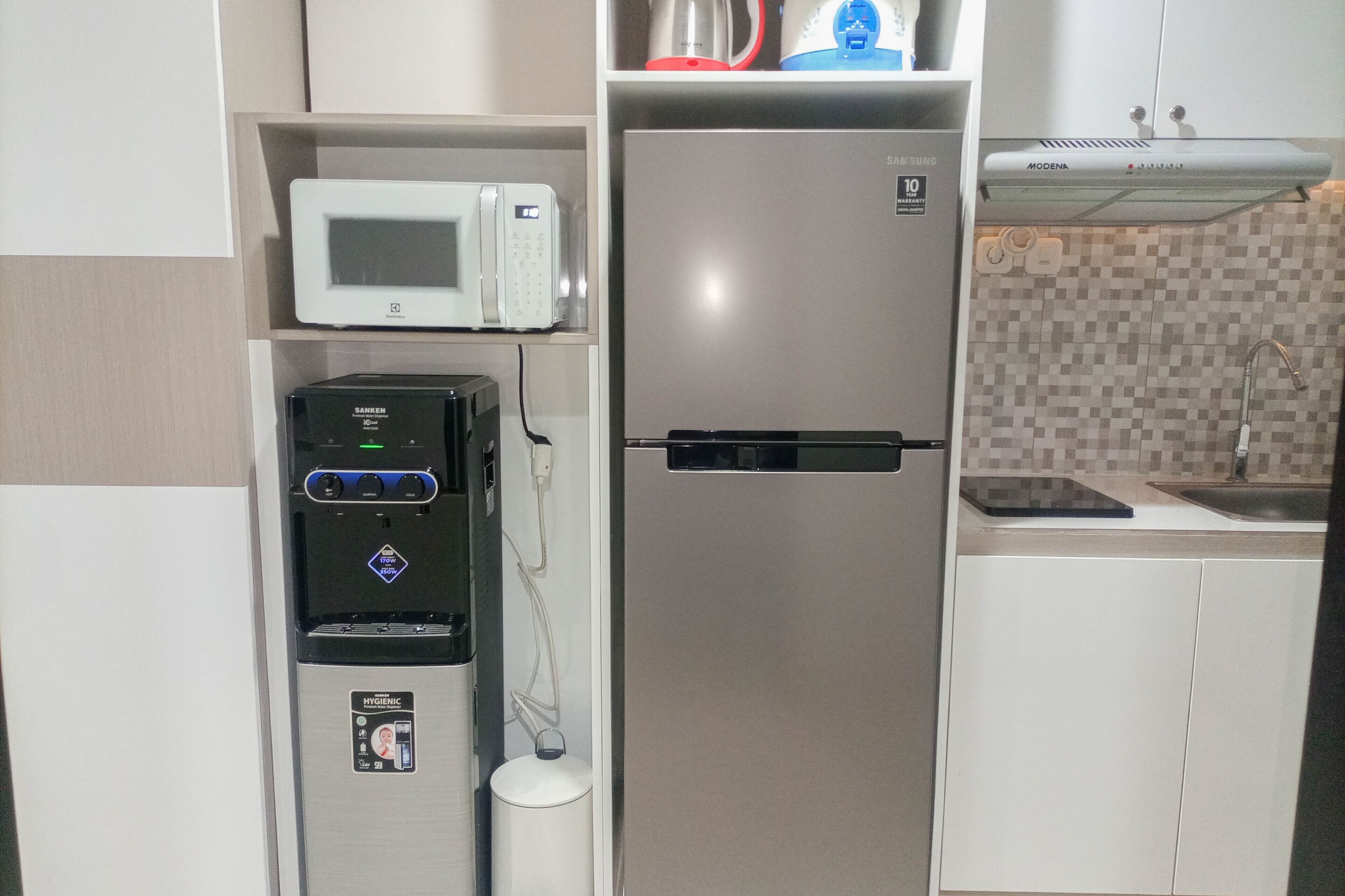 A compact kitchenette with a microwave, refrigerator, water dispenser, and a small sink.