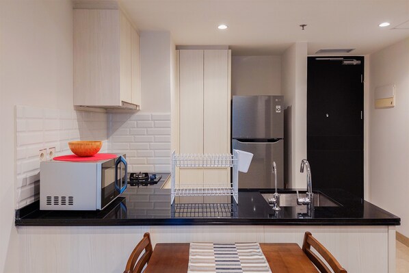 A modern kitchen with a black countertop, stainless steel appliances, and a white backsplash. - A Luxury 1BR Bali Style Apartment at Branz BSD City (Pagedangan)