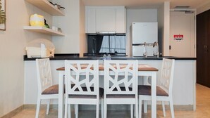 A modern kitchen with white cabinets, a black countertop, and a dining area with white chairs and a wooden table. - Nice And Spacious 2Br With Extra Room At Branz Bsd City Apartment (Pagedangan)
