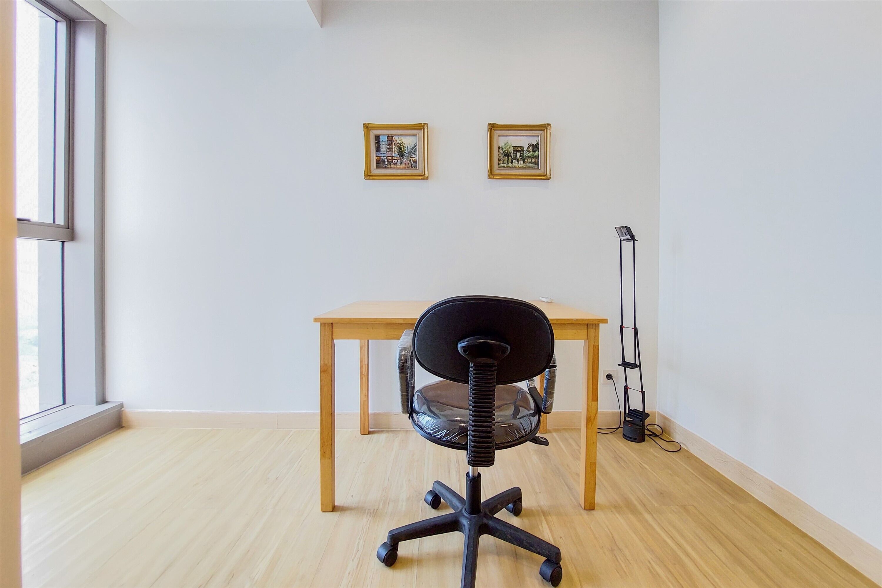A room with a wooden desk, a black office chair, and two framed pictures on the wall.