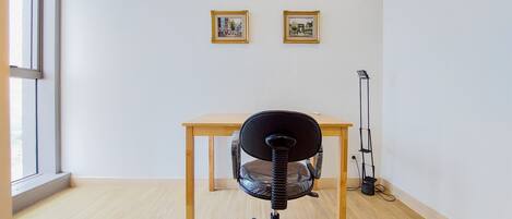 A room with a wooden desk, a black office chair, and two framed pictures on the wall.