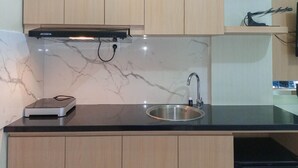 A kitchen with a black countertop, a stainless steel sink, wooden cabinets, a black range hood, and a dishwasher.