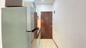 Ein schmaler Flur mit einem Kühlschrank links und einer Tür am Ende.