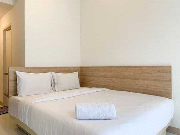 A neatly made bed with white linens and a wooden headboard in a hotel room.