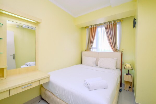 Una habitación de hotel con cama, mesita de noche, lámpara y ventana con cortinas.