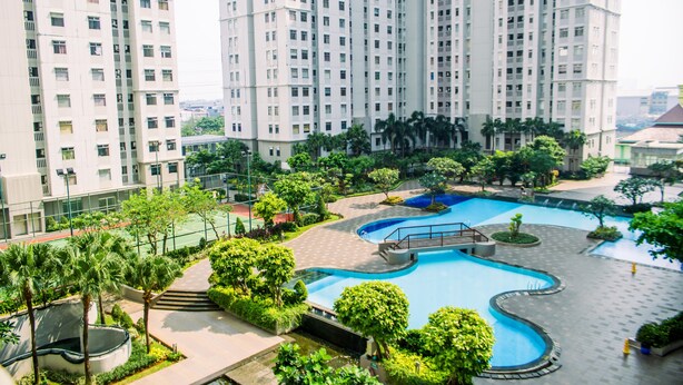 Un edificio residencial alto con múltiples balcones, piscina y zonas verdes circundantes.
