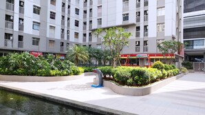Un edificio moderno de varios pisos, con balcones y un área ajardinada con plantas y una fuente.