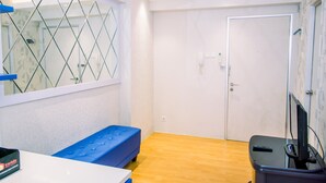 Una habitación con suelo de madera, un sofá azul, un escritorio con ordenador y un televisor sobre un mueble bajo.