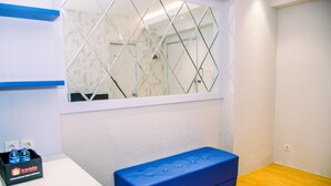 Una habitación con un banco azul, un ventanal con un espejo de diseño geométrico y una pequeña mesa con una botella de agua.