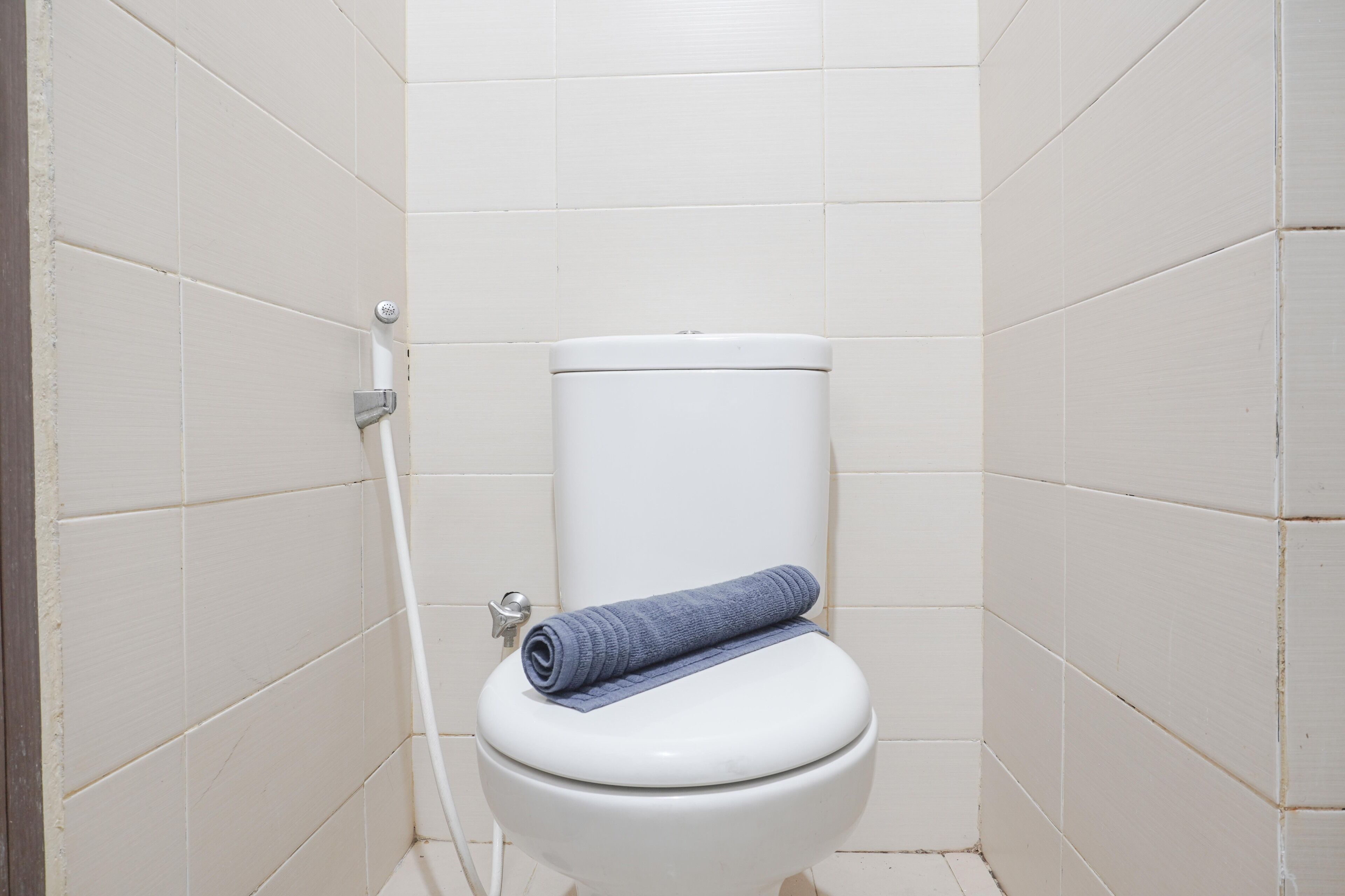 Des toilettes blanches avec une serviette bleue posée sur la lunette, le tout adossé à un mur carrelé.