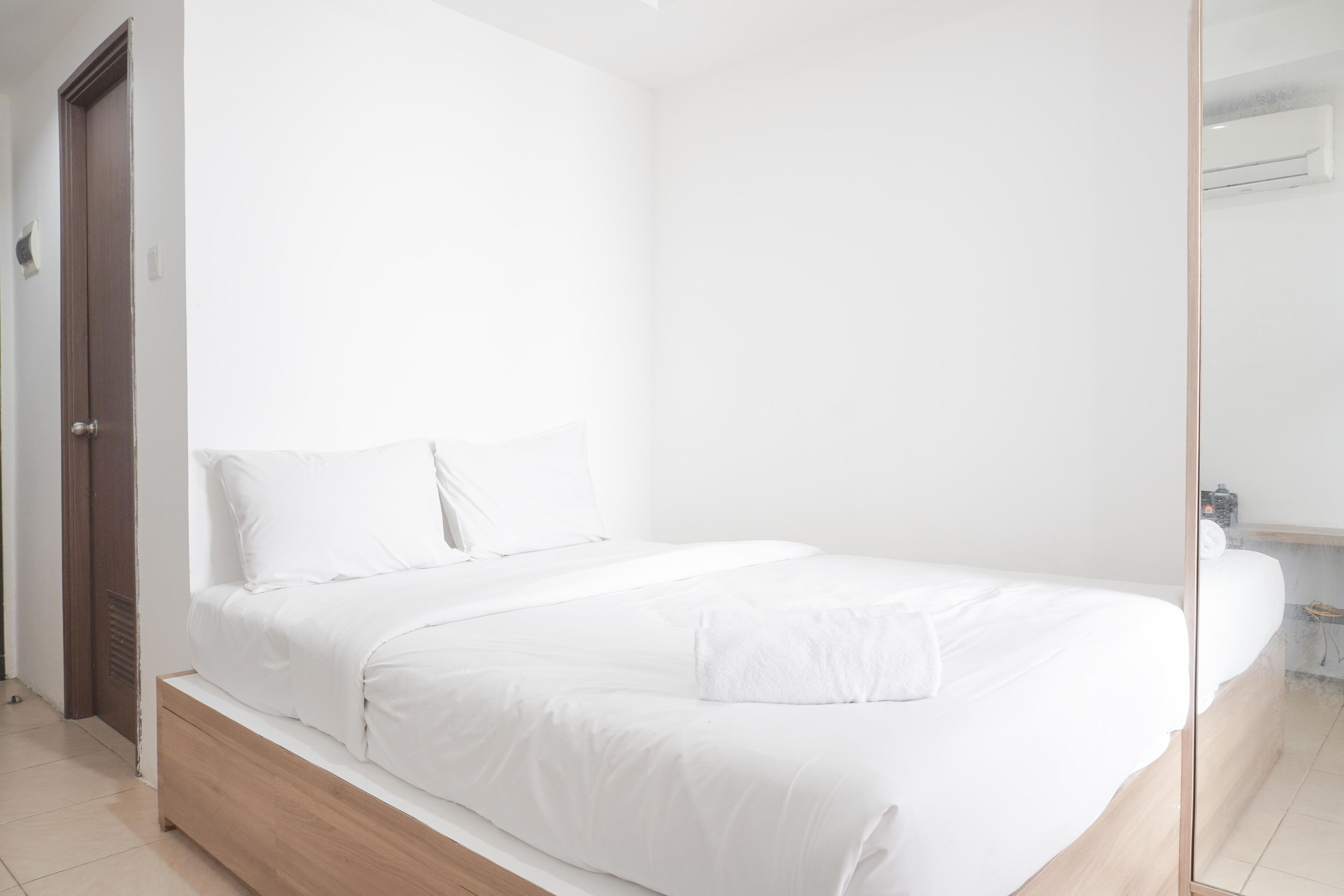 A minimalist bedroom with a single bed, a wooden nightstand, and a white wall.