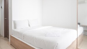 A minimalist bedroom with a single bed, a wooden nightstand, and a white wall. - Minimalist And Comfort Studio At Belmont Residence Puri Apartment (Jakarta)