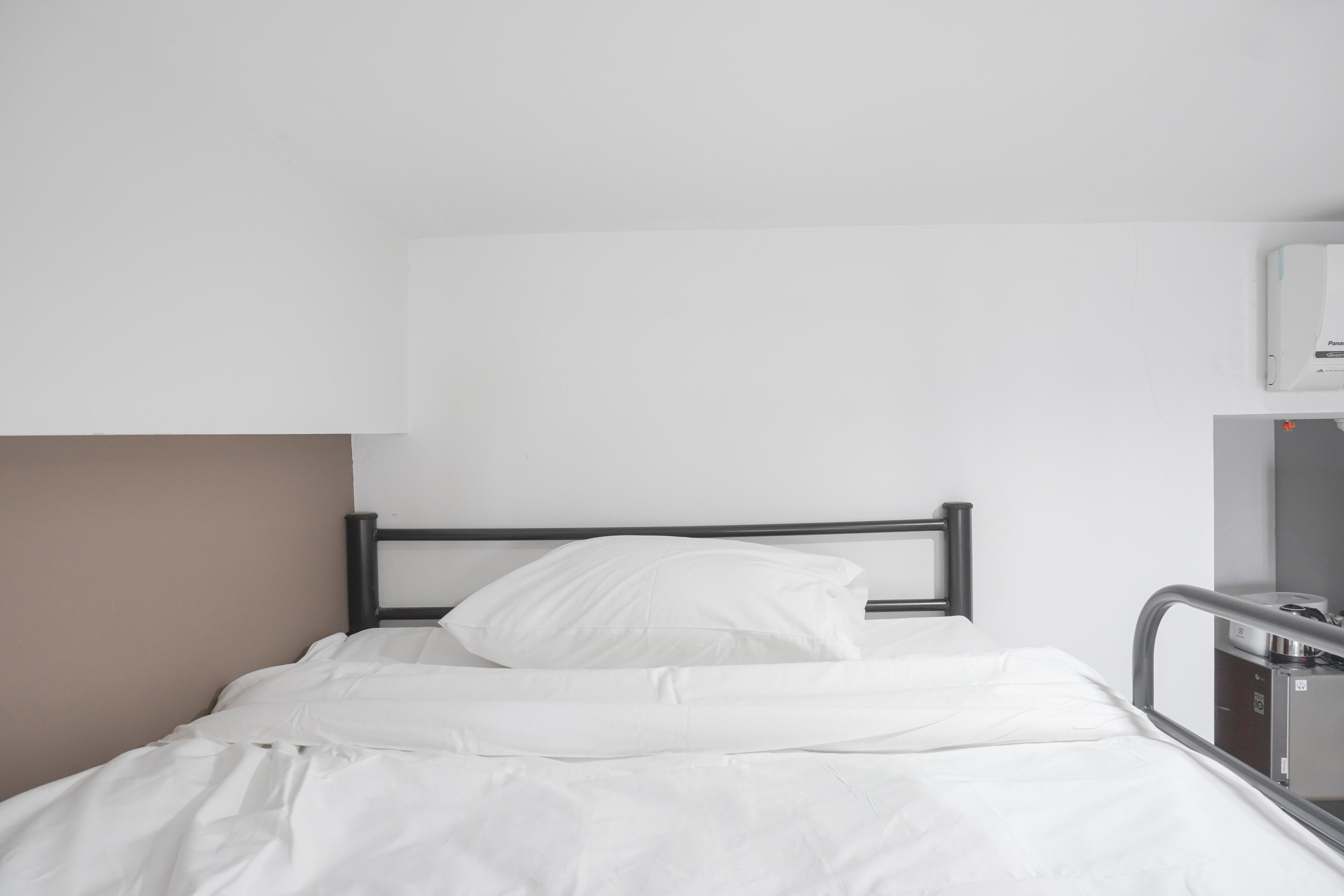 A single bed with white bedding, a metal headboard, and a bedside table with a lamp.