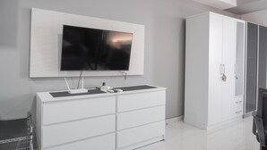 Een moderne kamer met een grote flatscreen televisie aan de muur, een witte dressoir met lades en een grote witte garderobe met glazen deuren.