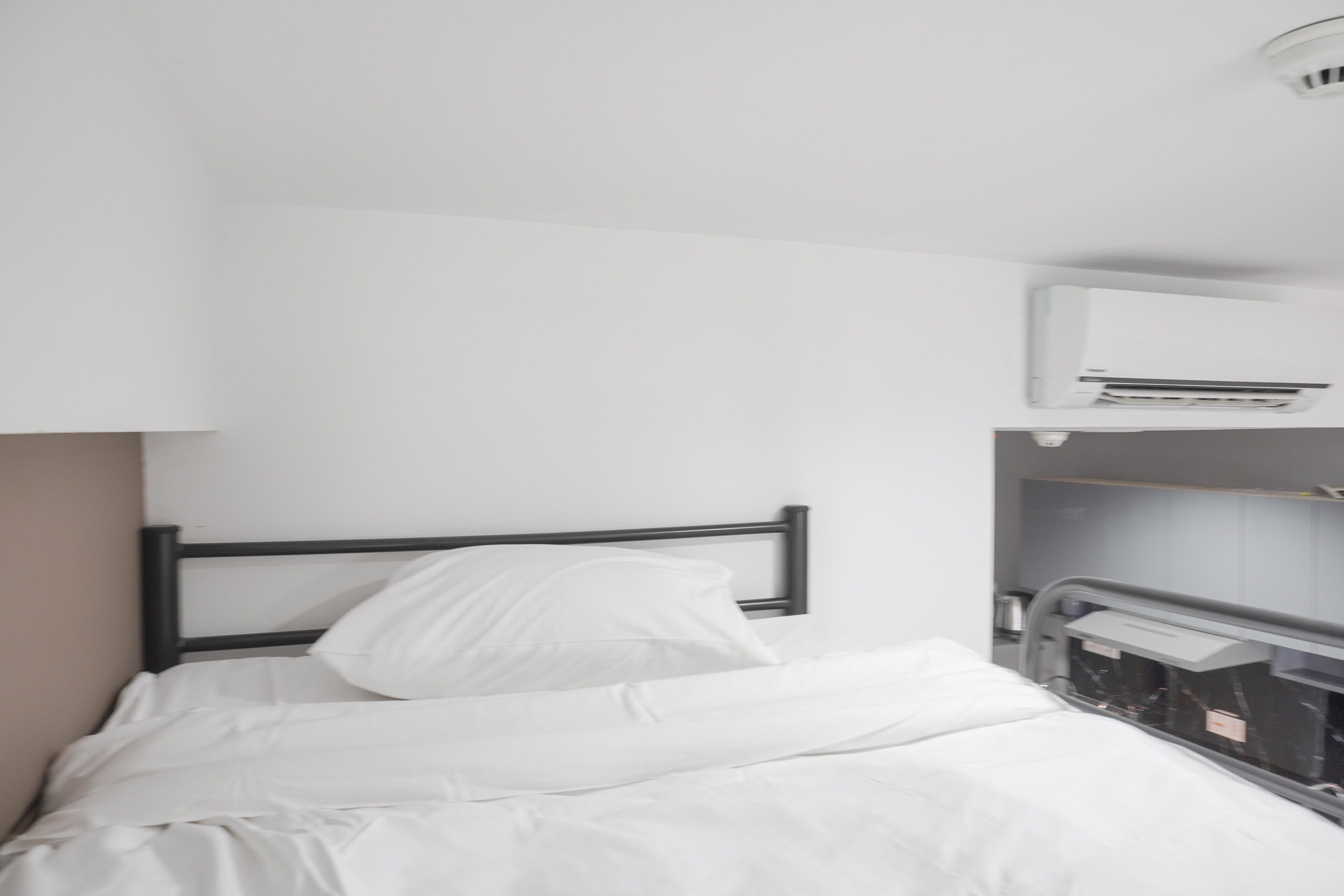 A single bed with white bedding and a black headboard in a room with white walls.