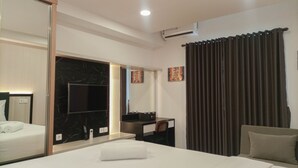 A hotel room with a bed, a desk with a chair, a mirror, and a window with curtains. - Comfy And Easy Access 2Br Apartment At Tanglin Supermall Mansion (Surabaya)