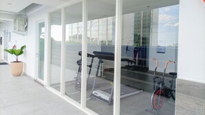 A modern indoor gym with exercise equipment, large windows, and a potted plant. - Comfy And Easy Access 2Br Apartment At Tanglin Supermall Mansion (Surabaya)