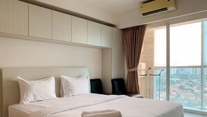 Ein ordentlich bezogenes Bett mit weißen Leinen und einem gefalteten Handtuch, ein Fenster mit Vorhängen und Blick auf die Stadt.