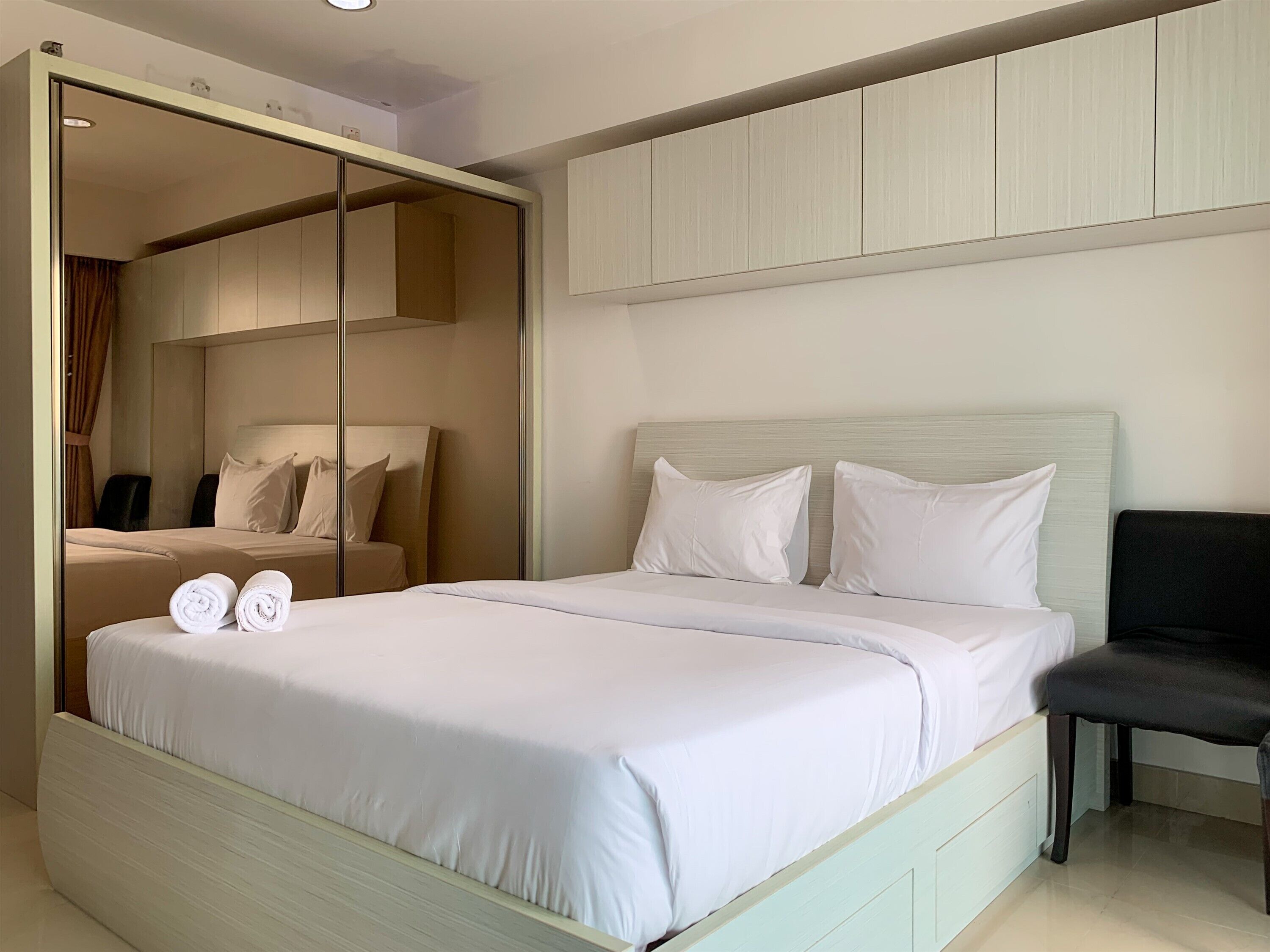 A modern hotel room with a large bed, a seating area with a chair, and a wardrobe with a mirror.