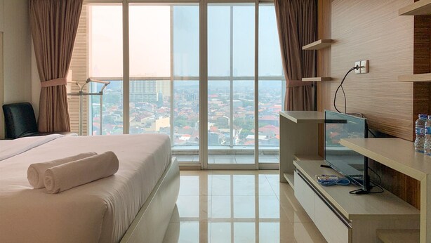 Ein Hotelzimmer mit einem Bett, einem Schreibtisch mit Computer, einem Fernseher und einem großen Fenster mit Vorhängen.