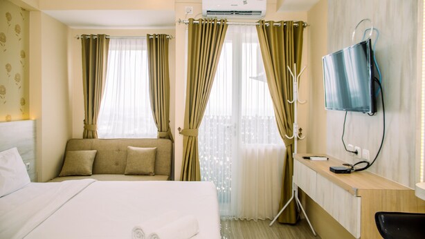 A hotel room with a bed, a desk, a chair, an air conditioning unit, and curtains. - Simple And Cozy Studio Apartment At Urban Heights Residences (South Tangerang)