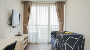 A room with a desk, a chair, a sofa, and a TV mounted on the wall. - Nice And Comfort 1Br At Casa De Parco Apartment (Pagedangan)