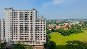 A high-rise building with multiple floors and balconies, surrounded by greenery and a residential area with houses and a park. - Nice And Comfort 1Br At Casa De Parco Apartment (Pagedangan)