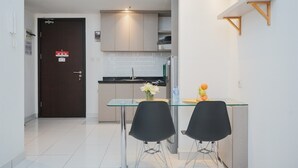 A modern kitchen with a glass dining table, two black chairs, and a small island with a vase of flowers. - Comfort And Simple 1Br At Casa De Parco Apartment (South Tangerang)