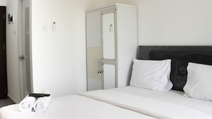 A hotel room with a bed, white linens, a remote control, and a door with a mirror. - Fancy And Nice Studio Apartment At Sayana Bekasi (Bekasi)