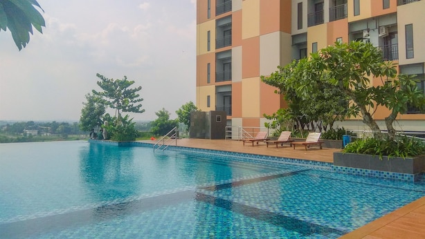 A swimming pool with tiled edges, surrounded by lounge chairs and greenery, adjacent to a multi-story building with balconies. - Fancy And Nice Studio Apartment At Sayana Bekasi (Bekasi)