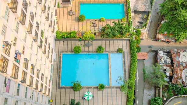 A rooftop swimming pool with two separate sections, surrounded by greenery and a multi-story building with balconies. - Fully Furnished And Comfy Studio Apartment Margonda Residence 3 (Depok)