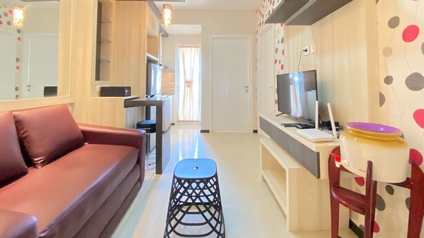 A modern living room with a sofa, a TV, a small table, and a chair. There is a kitchen area in the background. - Cozy And Serene 2Br Apartment At Parahyangan Residence (Bandung)