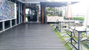 Un espace extérieur aménagé en terrasse, avec un sol en bois, une entrée en verre et des meubles de jardin comprenant des tables et des chaises.