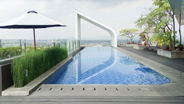 Une piscine à débordement située sur le toit, offrant une vue dégagée sur le paysage urbain, et entourée de verdure et d’une architecture moderne.