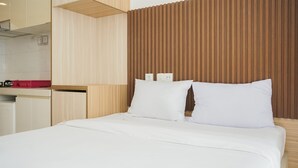 Habitación de hotel con cama, cabecero de madera y zona de kitchenette.