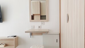 Una habitación minimalista con un tocador de madera, un espejo, un taburete pequeño y un armario.