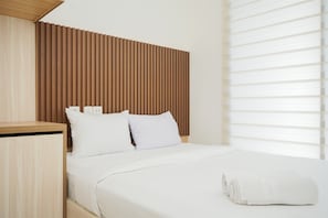 Quarto de hotel moderno com cabeceira de madeira, roupa de cama branca e cama bem arrumada com toalha enrolada.