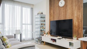 A modern living room with a large flat-screen TV, a glass display cabinet, and a wooden accent wall. - Minimalist And Cozy 1Br At Branz Bsd City Apartment (Pagedangan)
