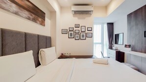 A modern hotel room with a large bed, a headboard, a wall-mounted air conditioner, and a series of framed pictures on the wall. - Minimalist And Cozy 1Br At Branz Bsd City Apartment (Pagedangan)